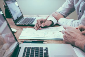 person holding pencil near laptop computer